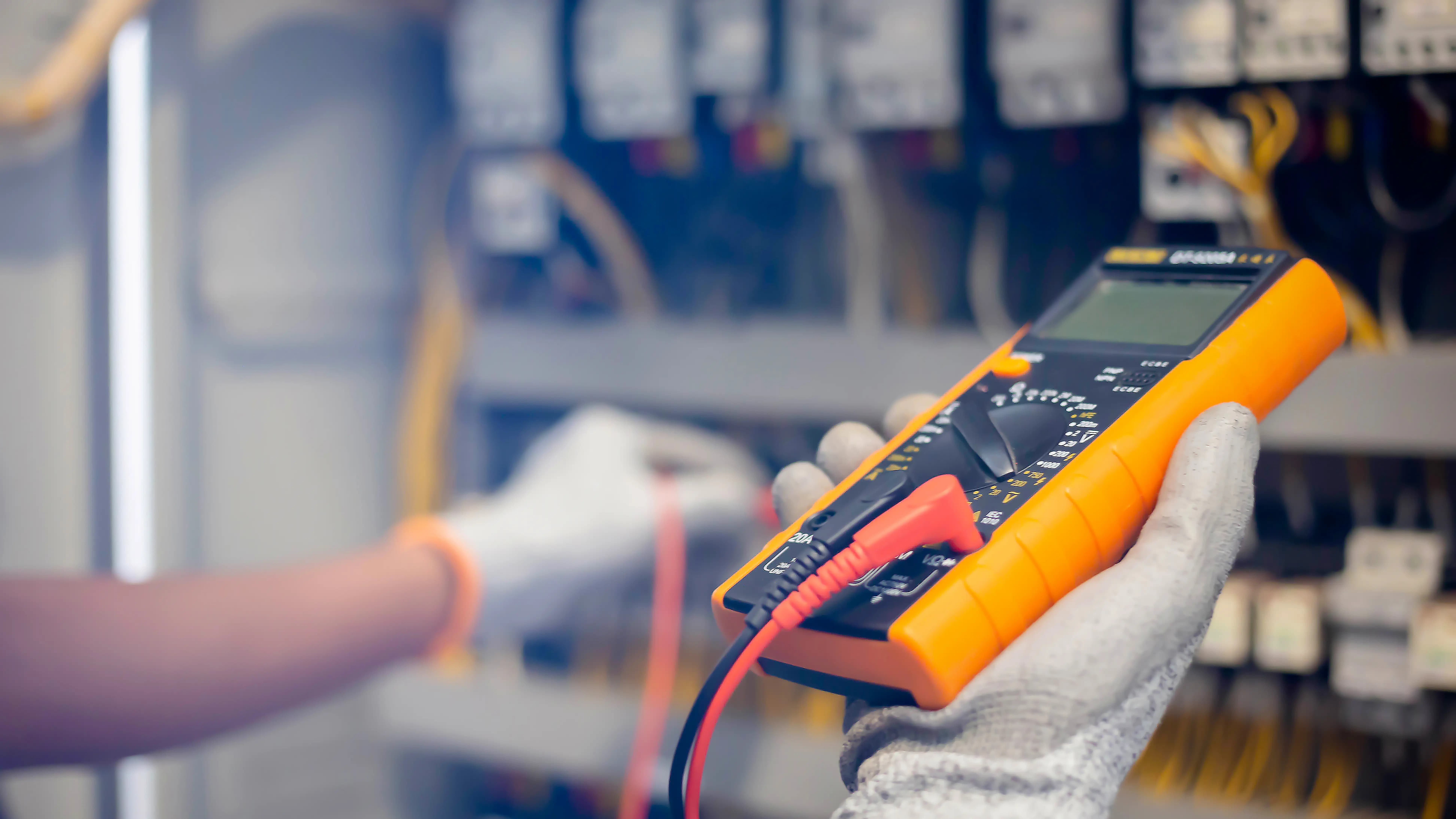 Electrician engineer uses a multimeter to test the electrical installation and power line current in an electrical system control cabinet.